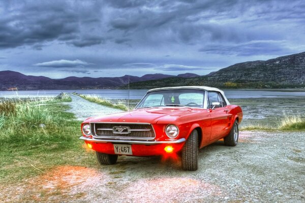 Czerwony Mustang nad jeziorem w pochmurną pogodę