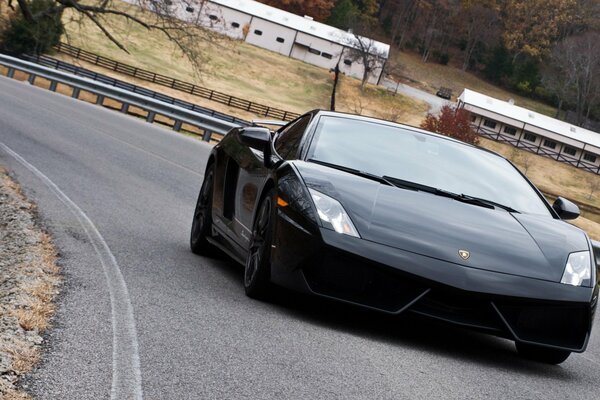 Czarny Lamborghini jedzie drogą z wybojami na krawędziach na tle jesiennego wiejskiego krajobrazu