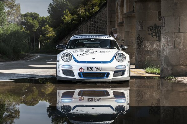 Białe Porsche odbija się w gładkim lustrze wody