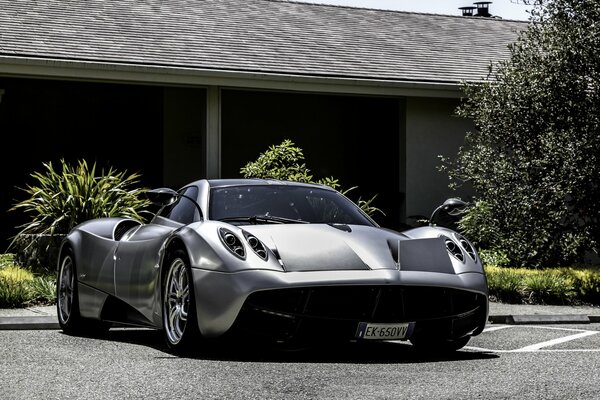 Серебристый красавец pagani huayra на фоне частного жилого дома