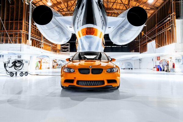 Pomarańczowe BMW pod samolotem w hangarze