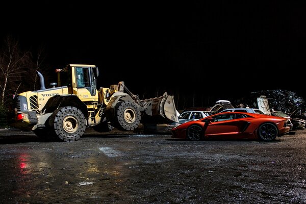Spychacz Volvo nocą z pomarańczowym Lamborghini