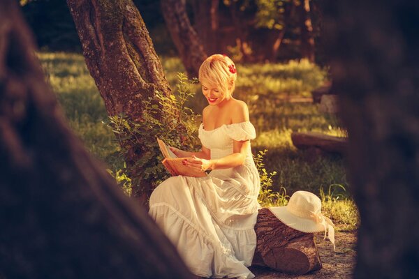 Симпотичная блондинка в белом платье читает книгу на природе