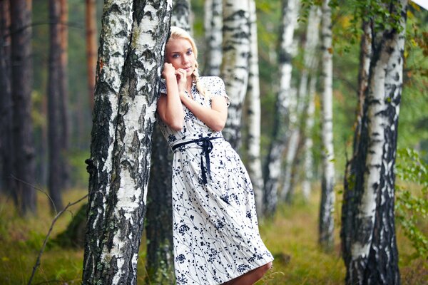 Piękna dziewczyna blondynka oparła się o brzozę
