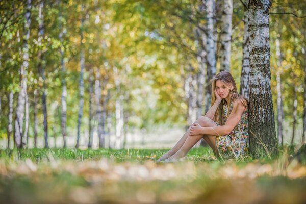 Dziewczyna w sukience siedząca przy drzewie w lesie